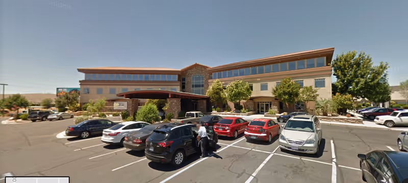A large modern senior care facility with a parking lot in front and several parked cars.