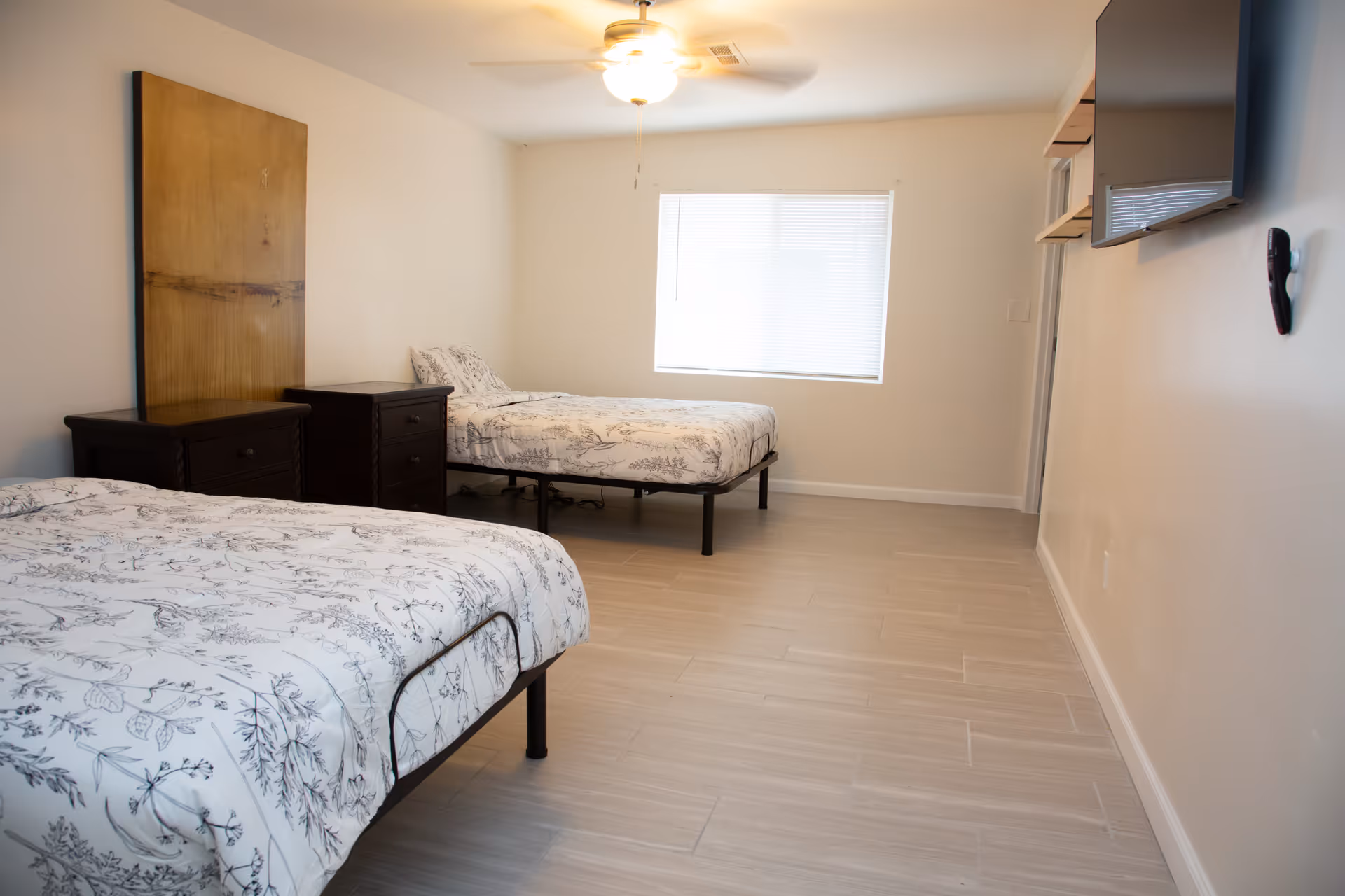 A sparsely furnished senior living bedroom with two beds, nightstands, and a window.