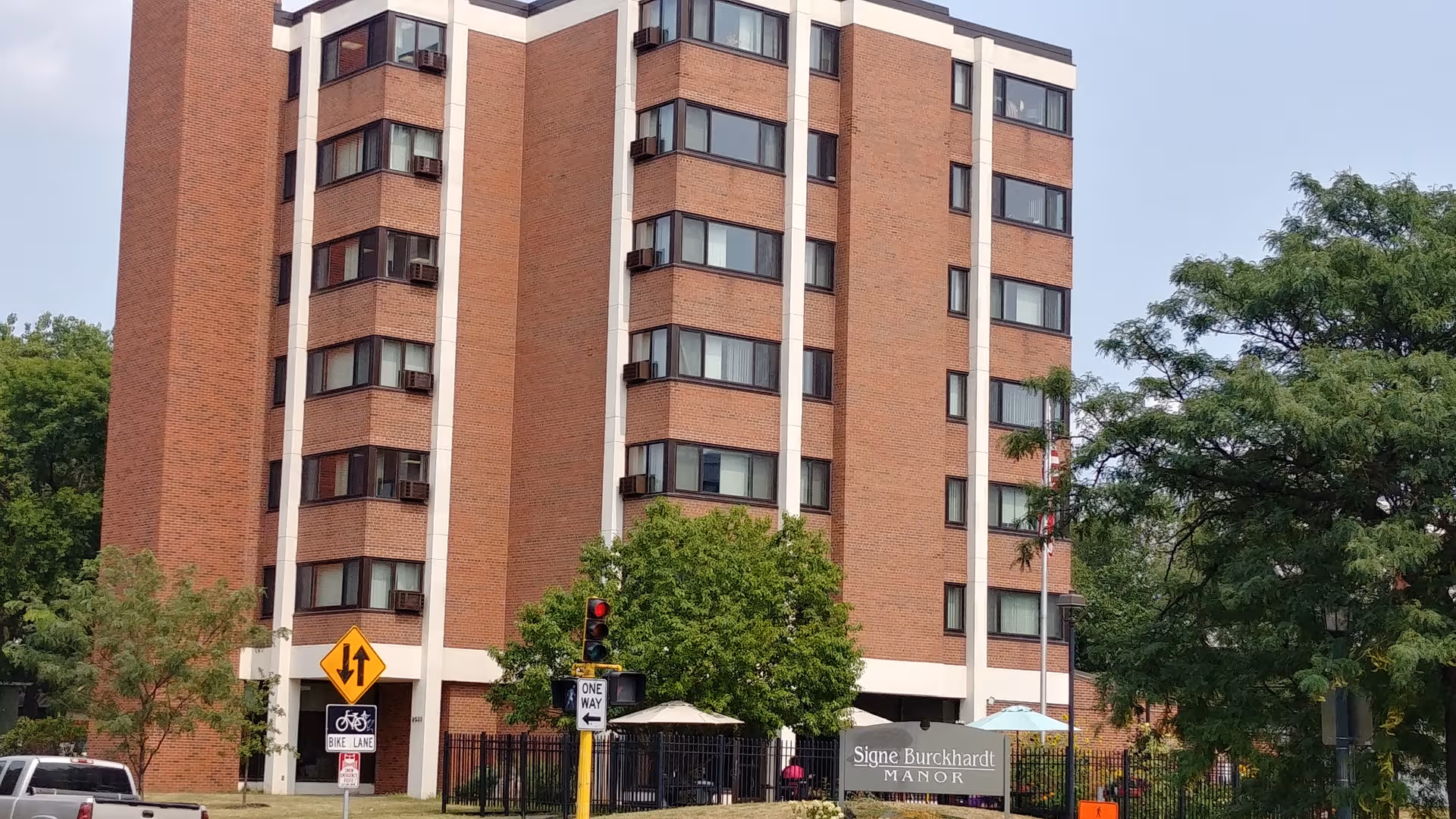 Tall brick senior living building with Signe Burckhardt Manor sign and outdoor seating