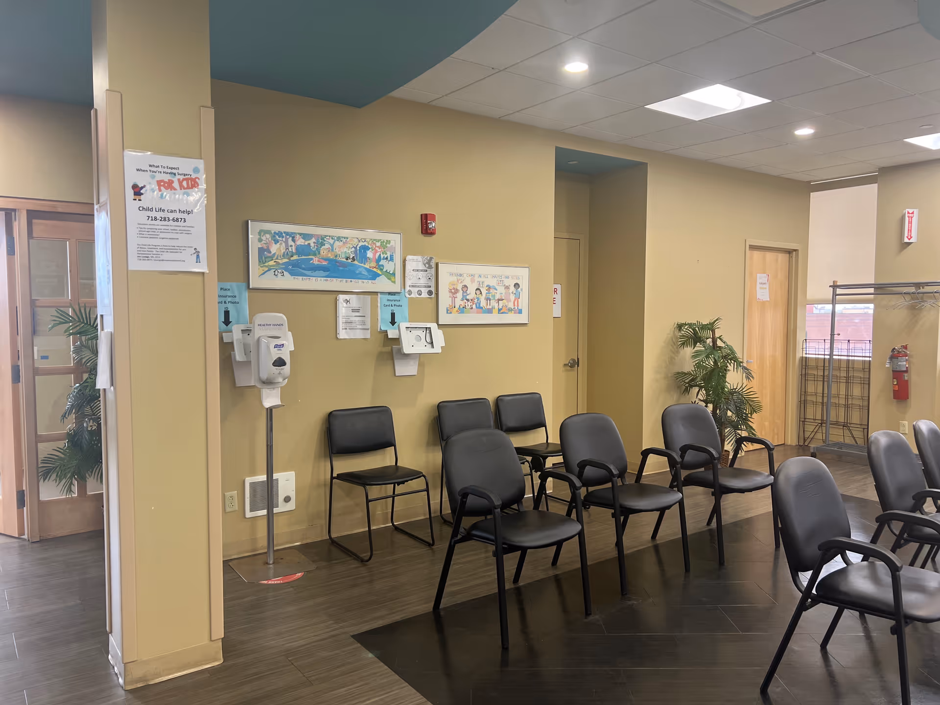 A waiting room area with rows of black chairs, posters, and a hand sanitizer station.