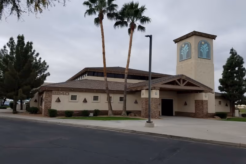 Sunland Springs Village building front with tower, palm trees, and a curbside driveway.