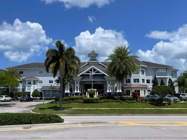 Front exterior view of Alto Stuart facility, a large multi-story building with a covered entrance, palm trees, and a well-maintained lawn under a partly cloudy blue sky.