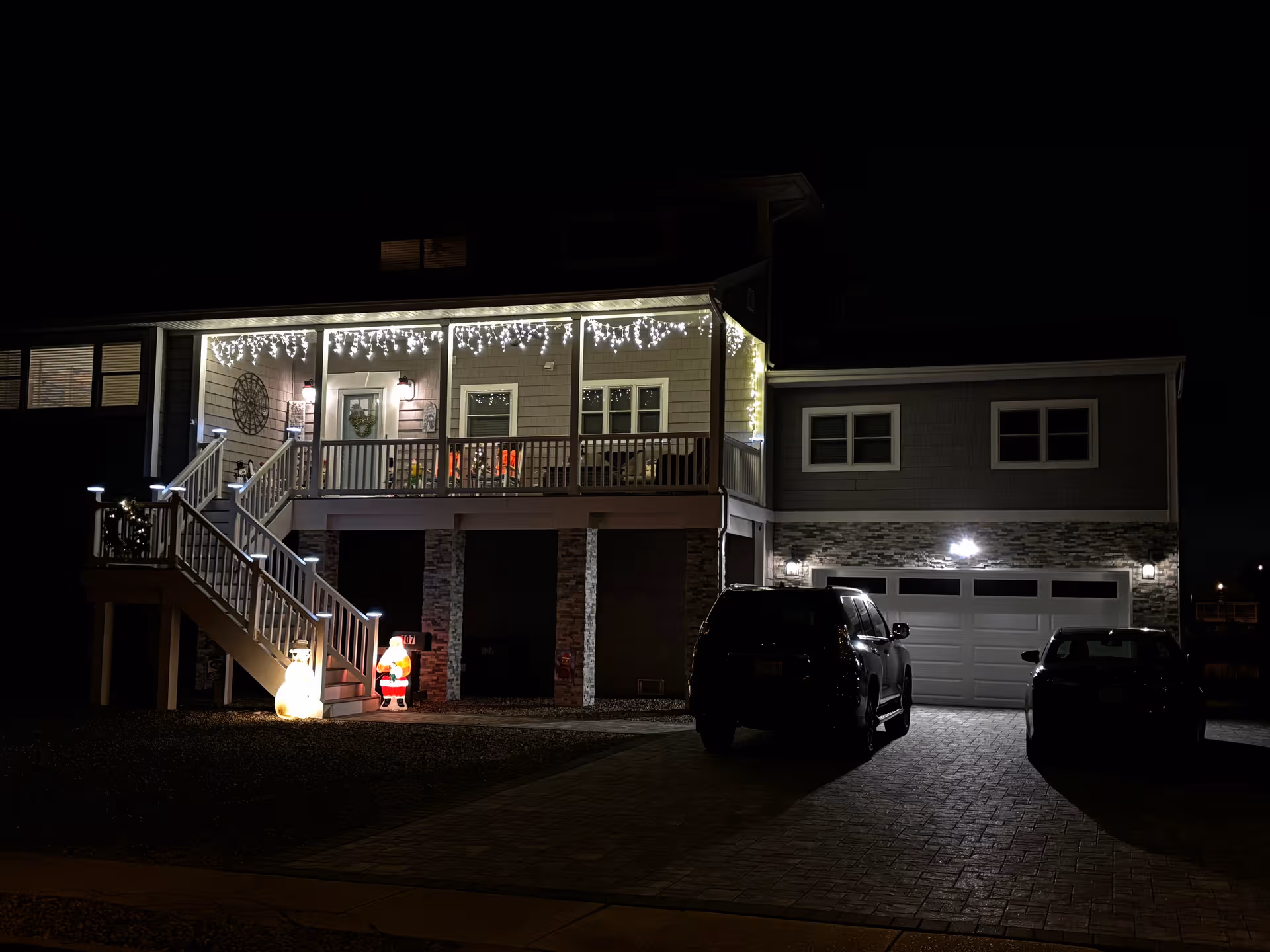 Nighttime exterior of Tritan House Rooming with porch lights, string lights, and parked cars.