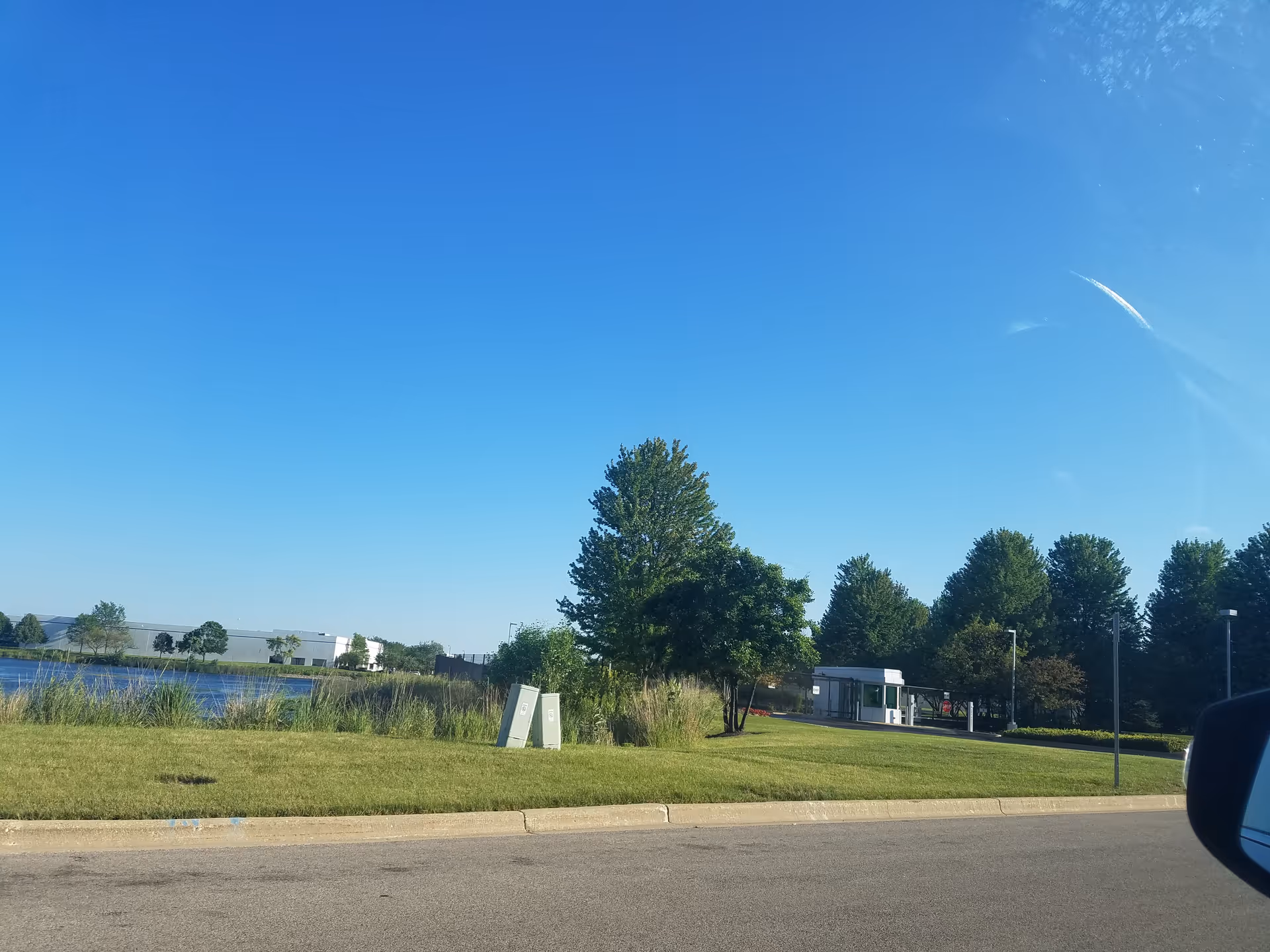Outdoor view of a grassy area with trees, a small building, and a water body.