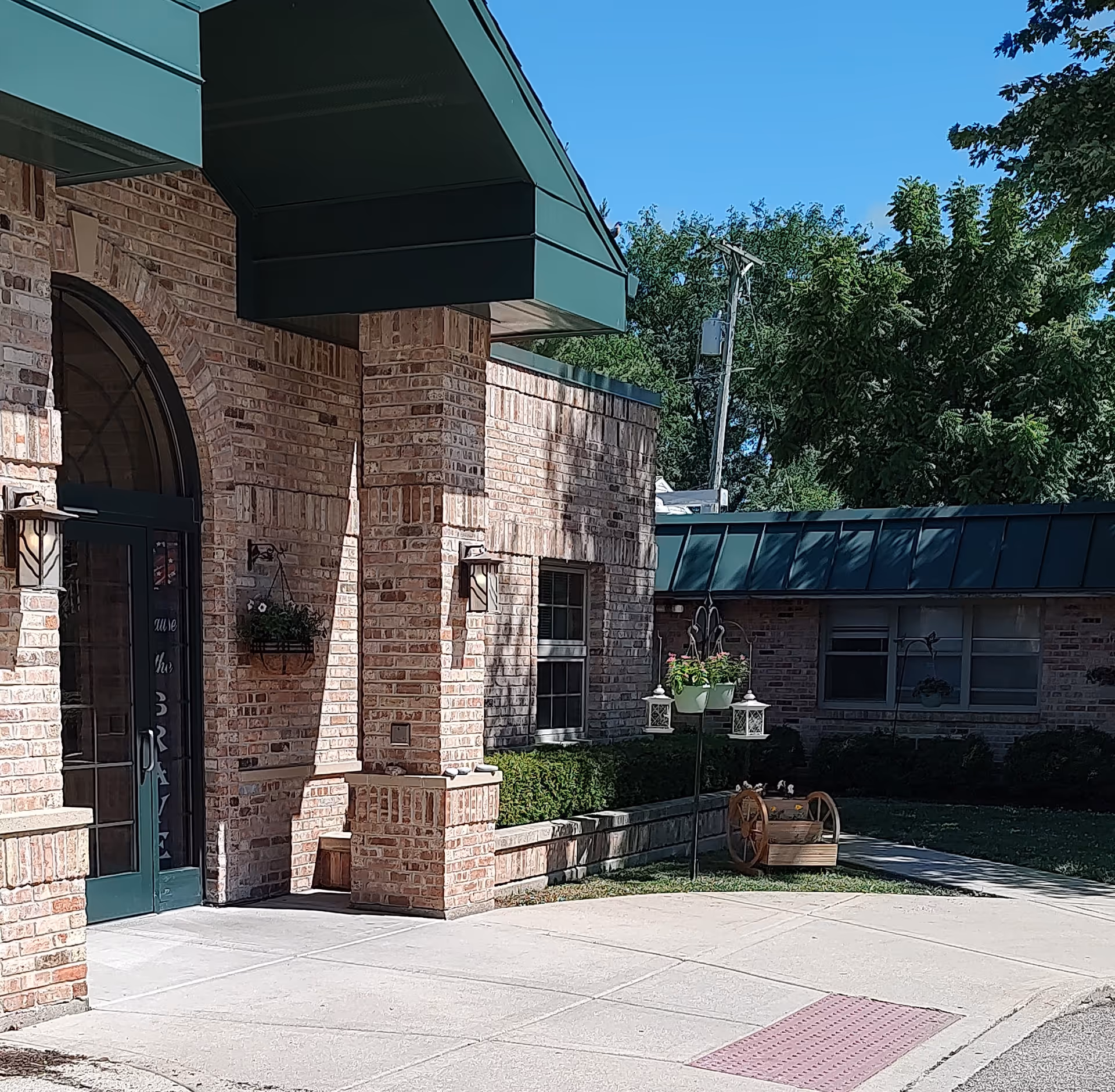 Brick senior living facility entrance with green awning, planters, and a paved sidewalk.