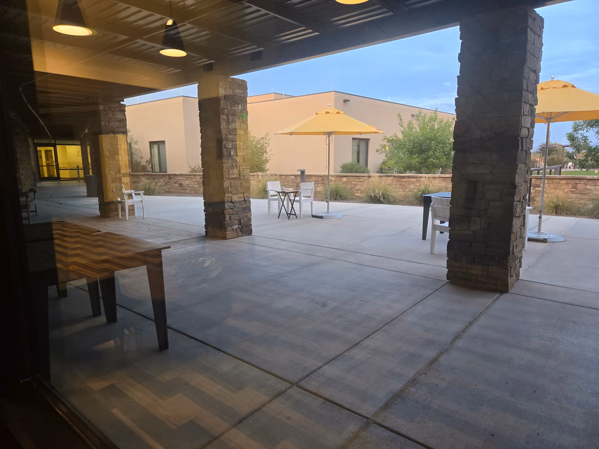 Covered outdoor patio with tables, chairs, and beige umbrellas.