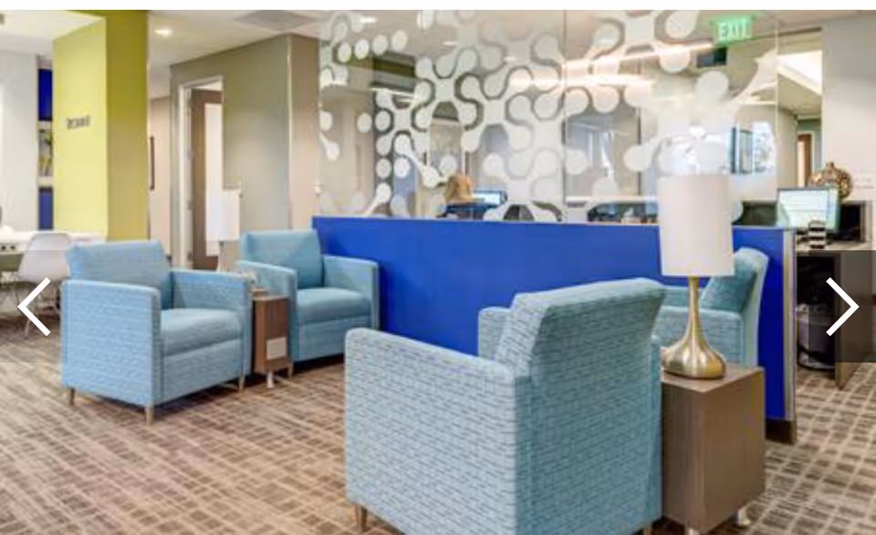 Modern lobby seating area with blue chairs, glass divider, and geometric wall pattern.