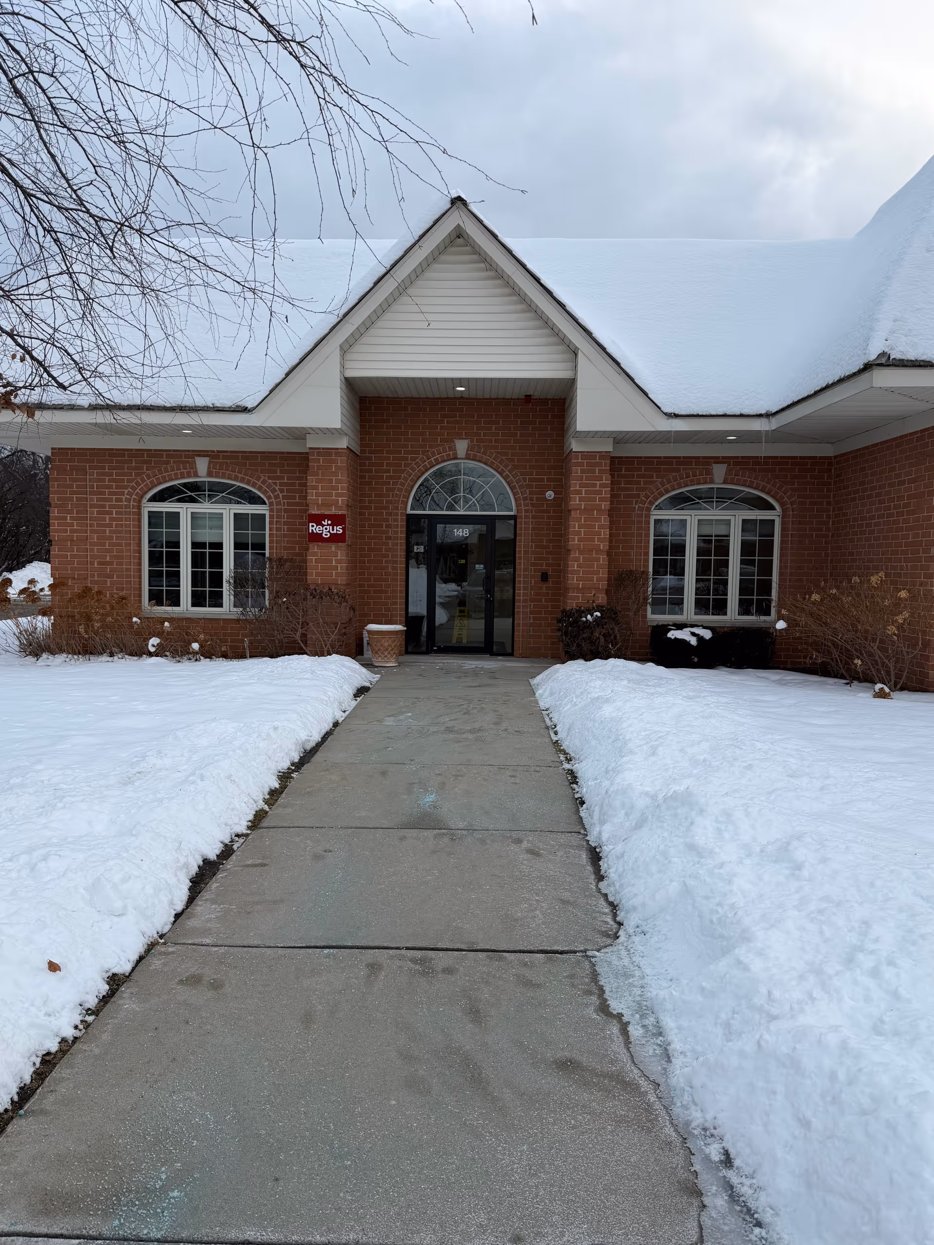 Winter scene of a brick facility entrance with snow-covered lawn and walkway.