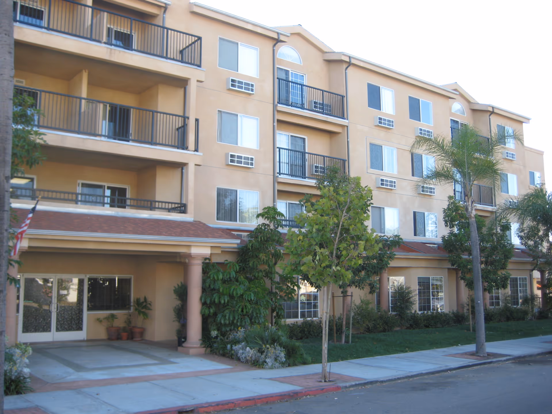 A peach-colored, multi-story senior living building with balconies and a landscaped entrance.