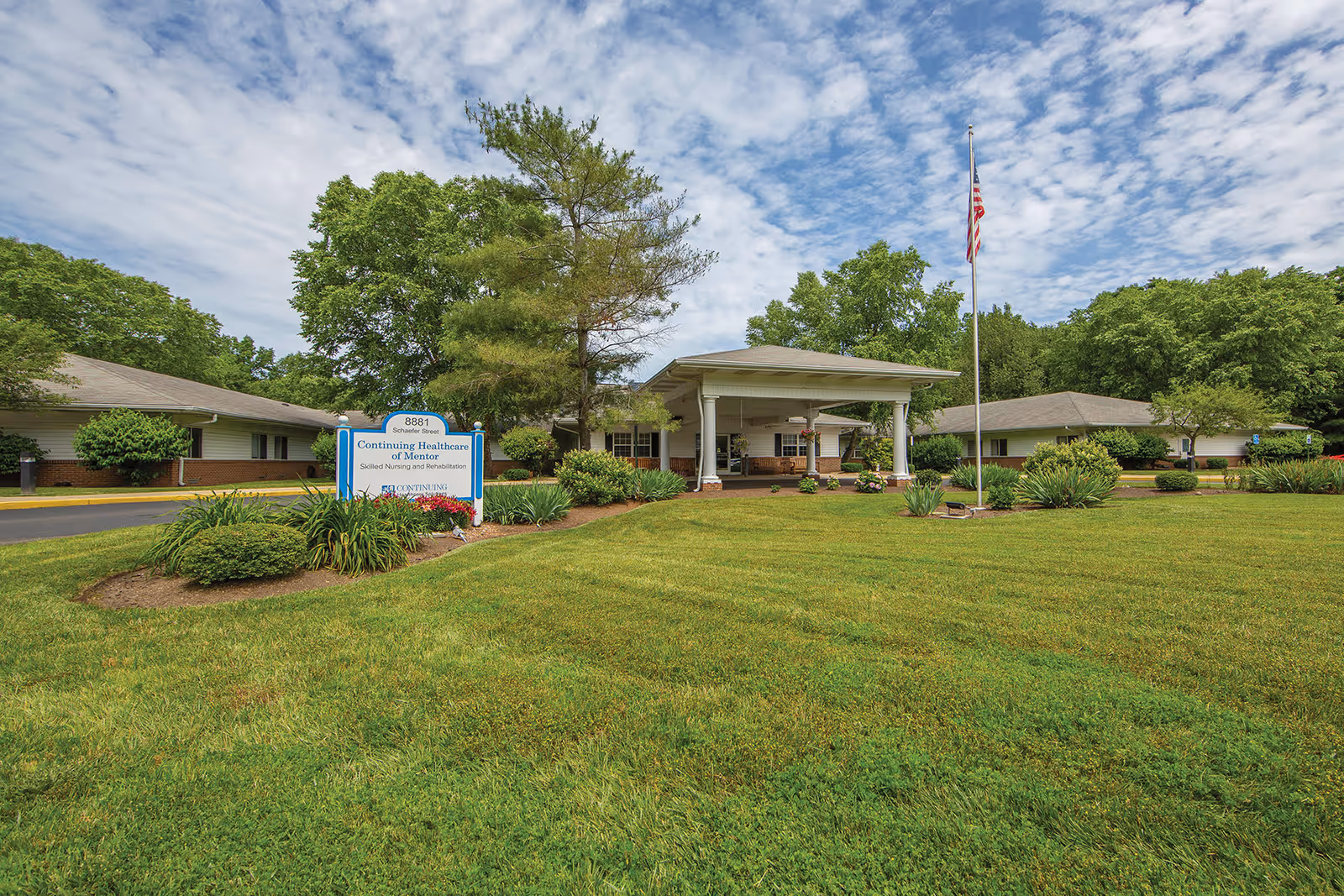 Exterior view of CareCore at Mentor with entrance canopy, sign, flagpole, and lawn.