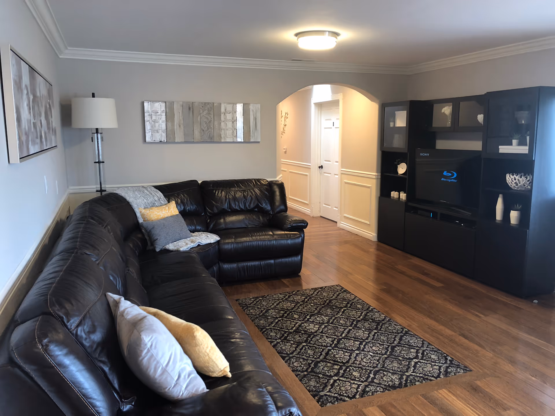 Cozy living room with a black leather sectional, wooden floors, and an entertainment center.