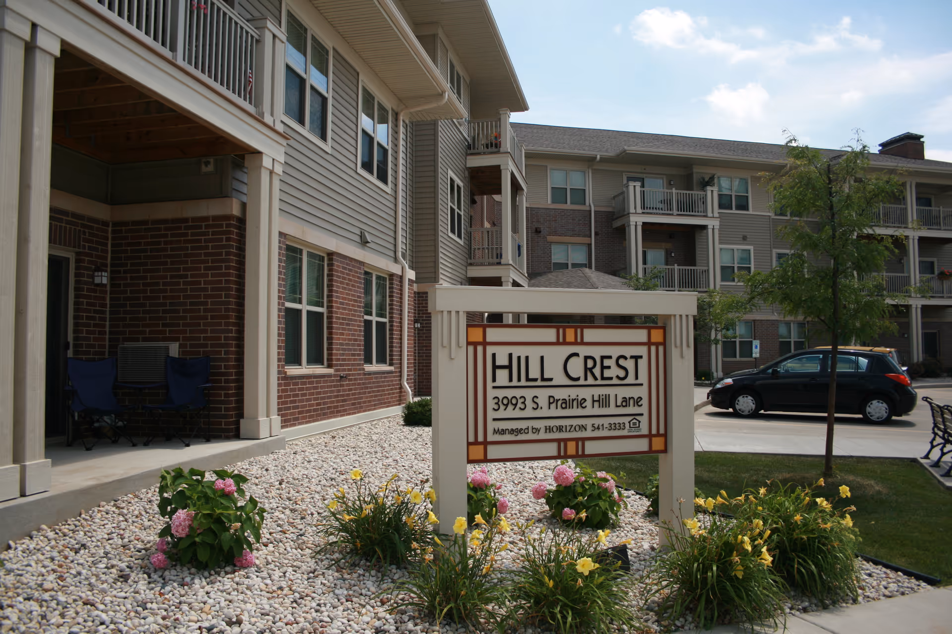 Exterior view of Hill Crest Apartments complex with a sign and landscaped front yard.