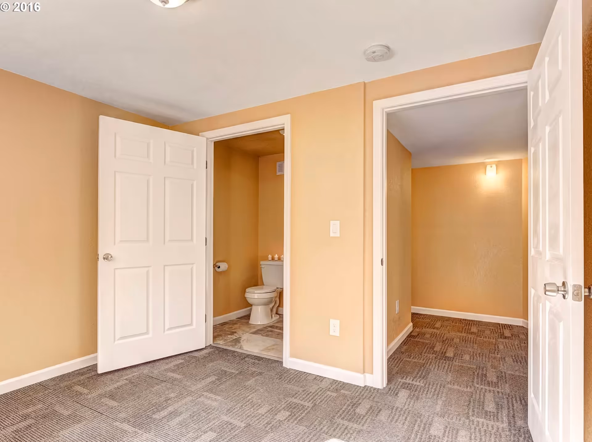 Beige-carpeted room with two open doors: one to a small toilet, the other to a hallway.