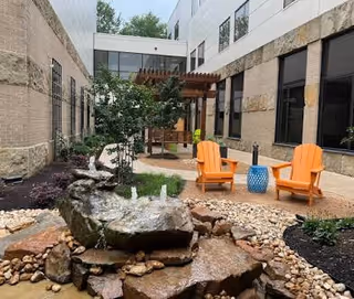 Outdoor courtyard with orange chairs, a water feature, rocks, and a wooden pergola.