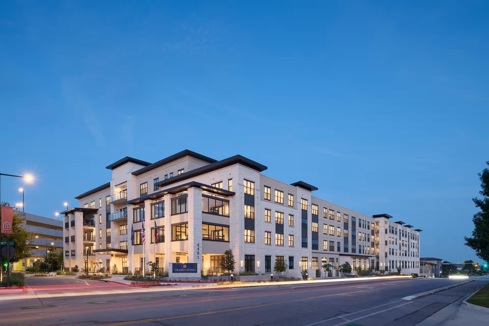Exterior view of a modern senior living building at dusk with lit windows.