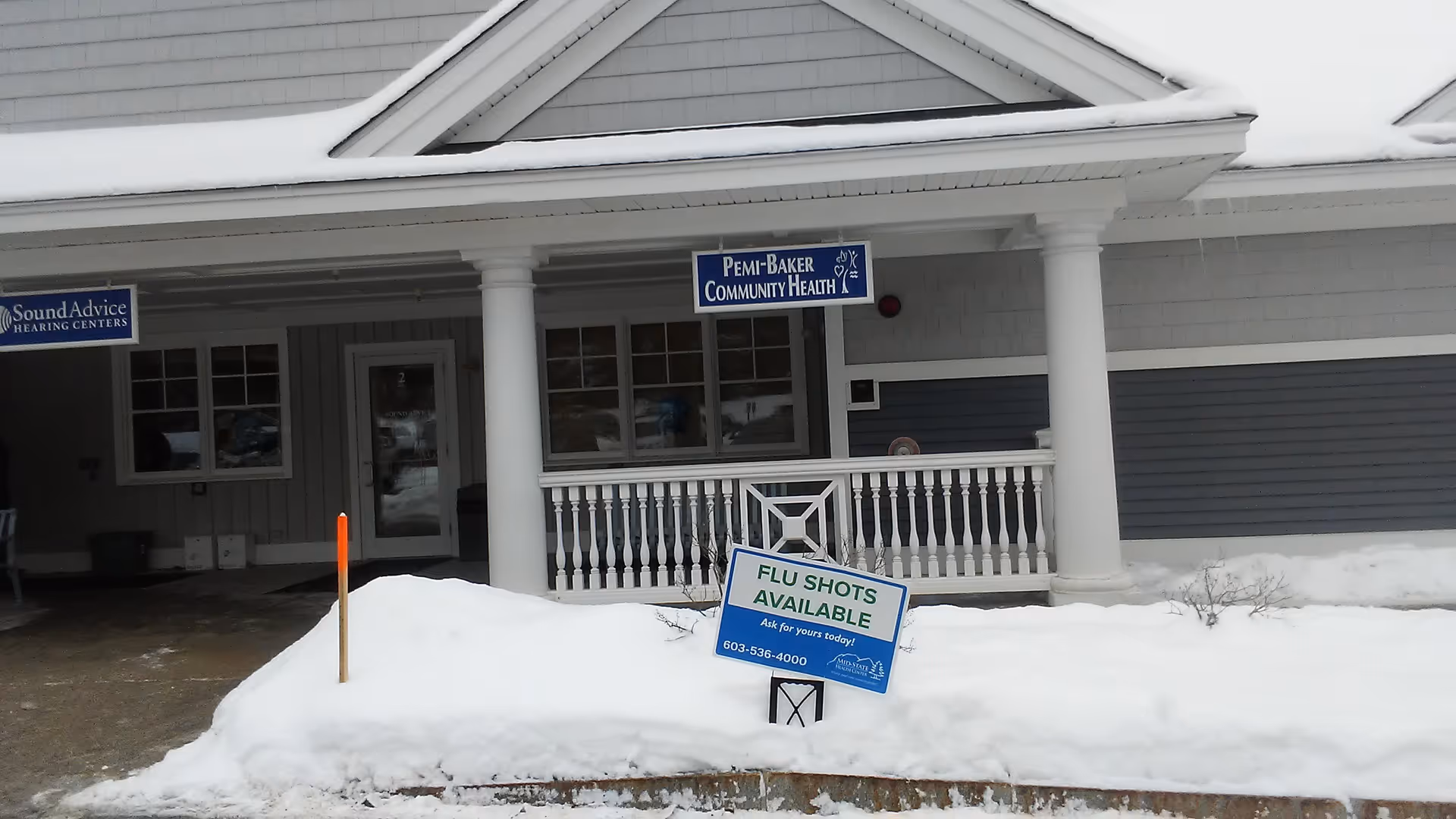 Snow-covered senior facility front entrance with porch columns and flu shots sign