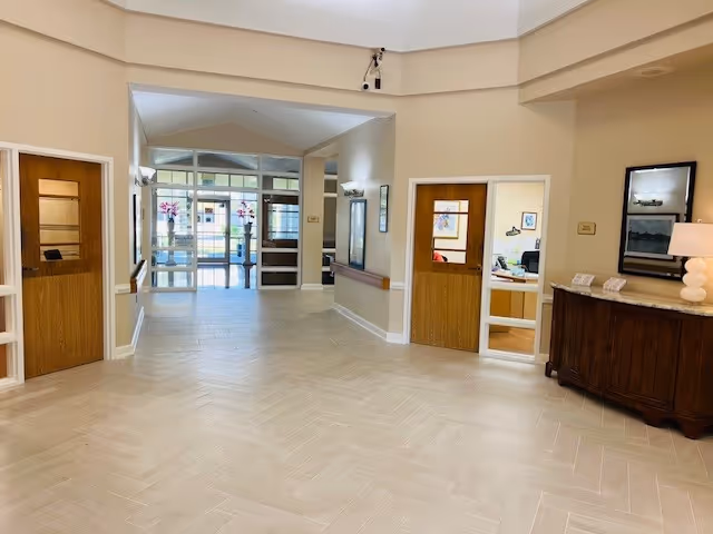 Bright nursing home lobby with a reception desk, hallways, and glass doors.