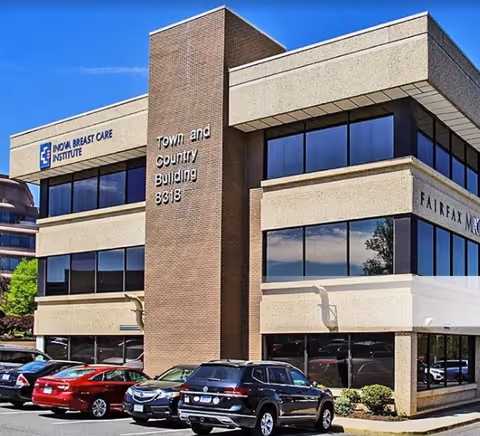 Modern office building exterior with glass windows and parking lot.