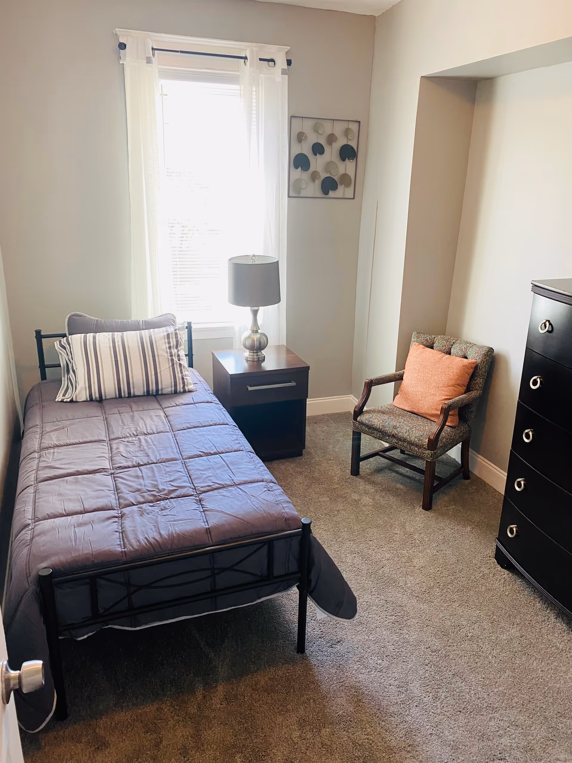 Small bedroom with a single bed, nightstand, lamp, chair, dresser, and a window.