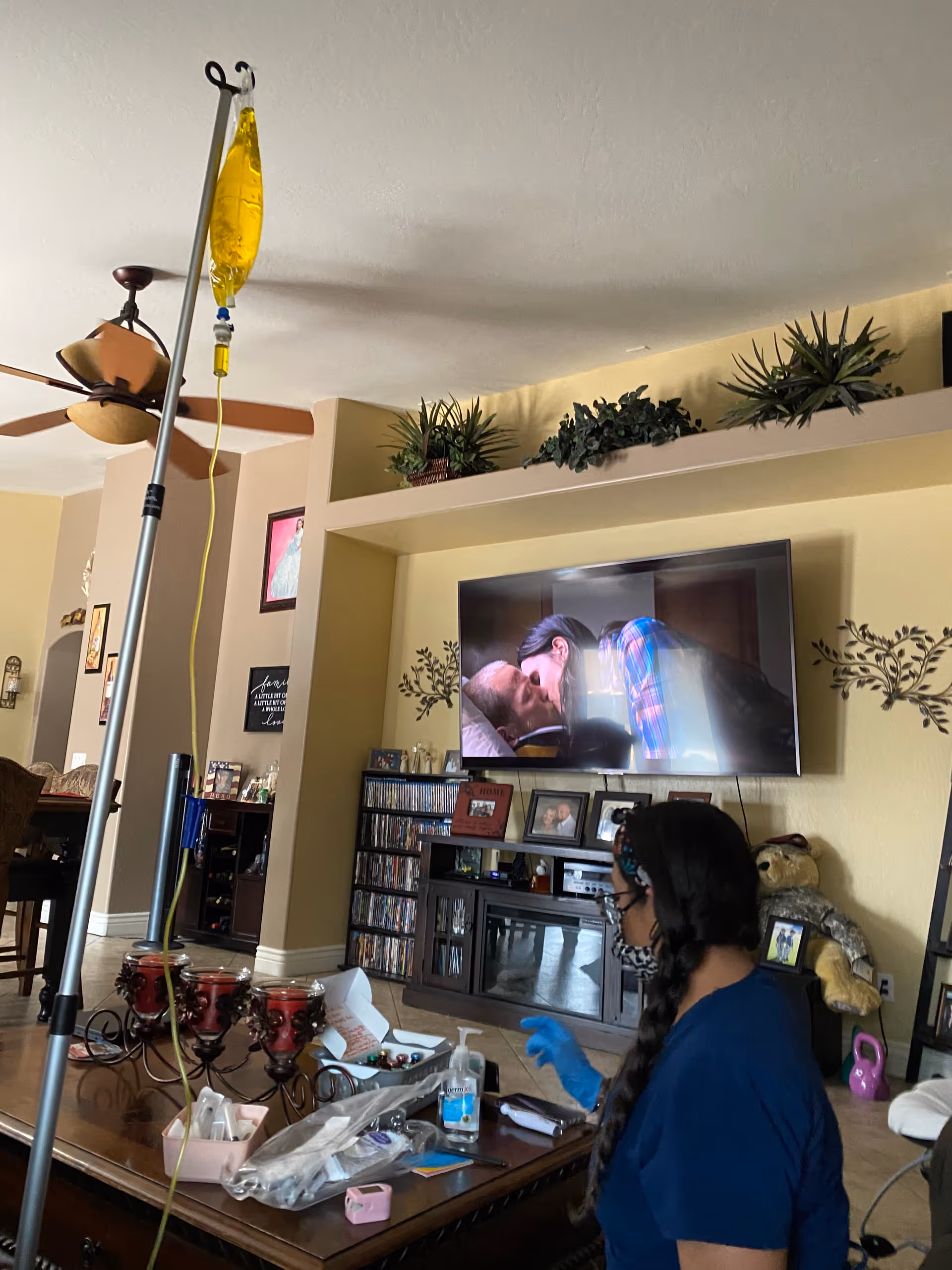 Nurse in blue scrubs provides care near an IV pole in a cozy living room.