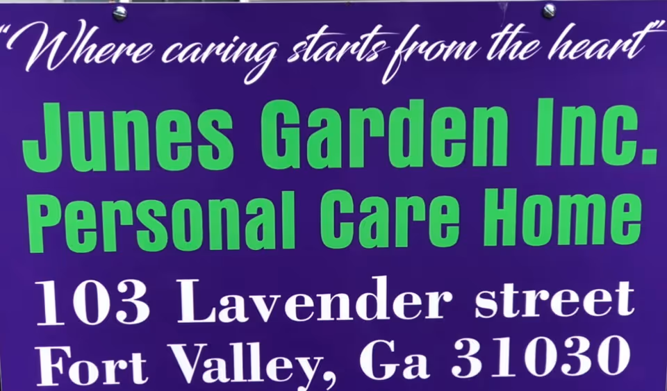 Purple exterior sign promoting June's Garden Inc. Personal Care Home with address.