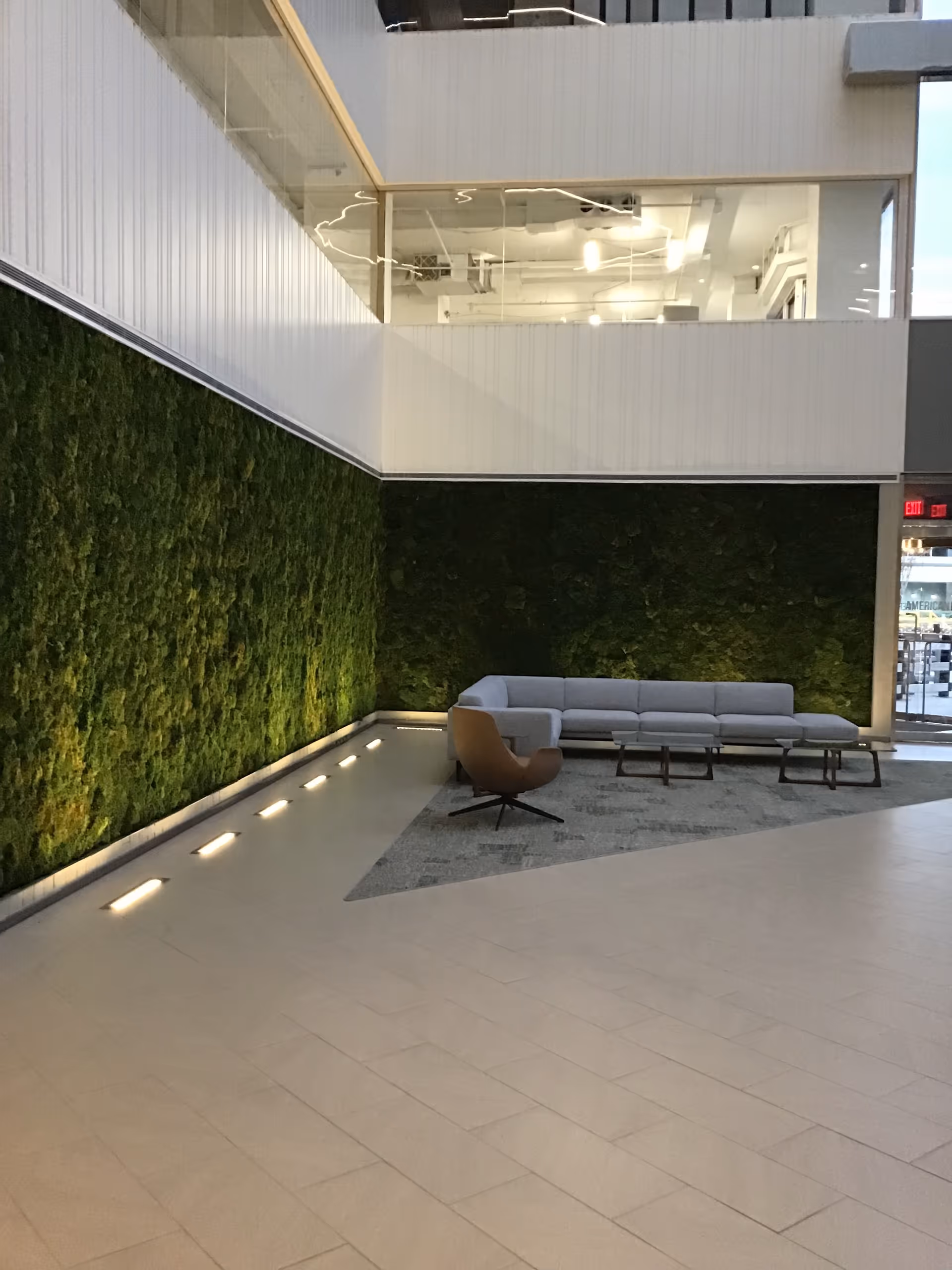 Contemporary indoor lobby with a green moss wall, gray sectional sofa, and a brown lounge chair.