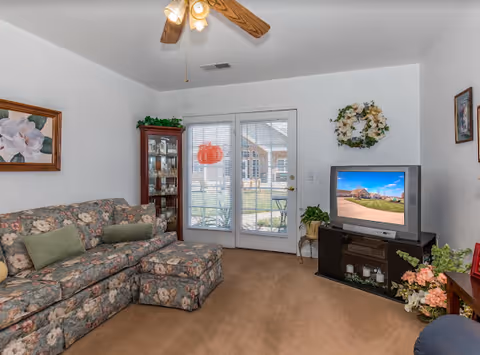 Cozy living room with floral sofa, TV stand, and glass doors opening to outdoors.