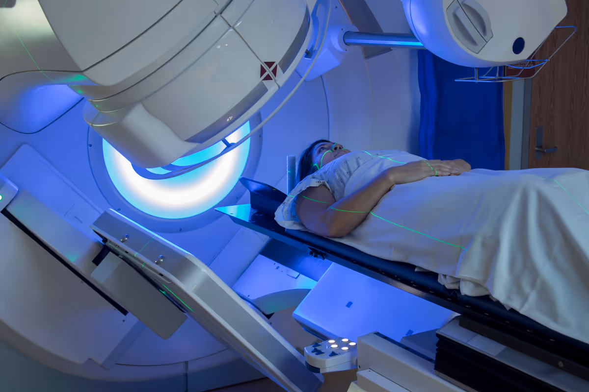 Patient lies on imaging table inside MRI scanner in a clinical radiology suite with blue lights.