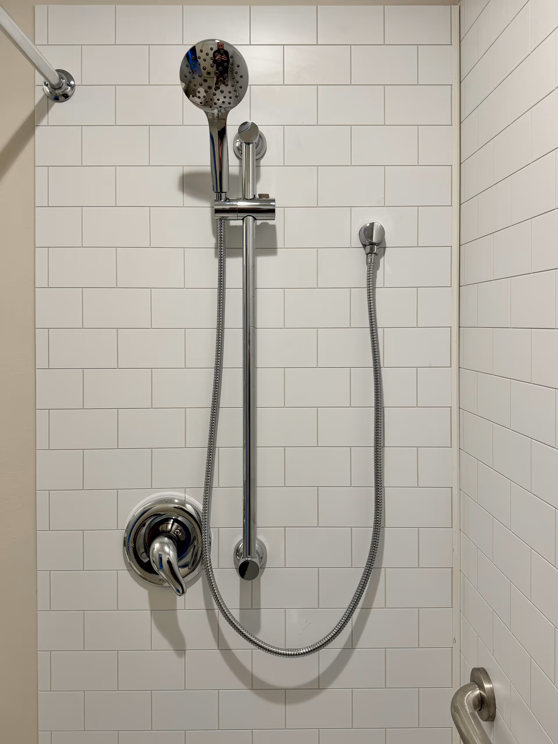 Shower with chrome fixtures and handheld showerheads against white tiled bathroom walls.