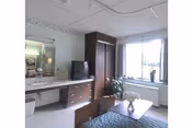 A furnished senior living bedroom with bed, dresser, wardrobe, and a large window.