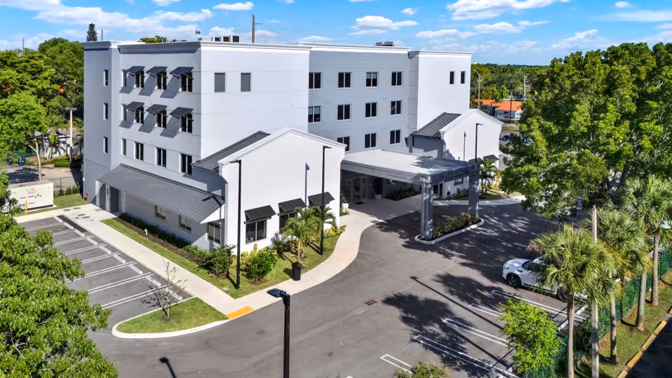 A modern white Sunset Point ALF exterior with a covered entrance and surrounding parking lot.