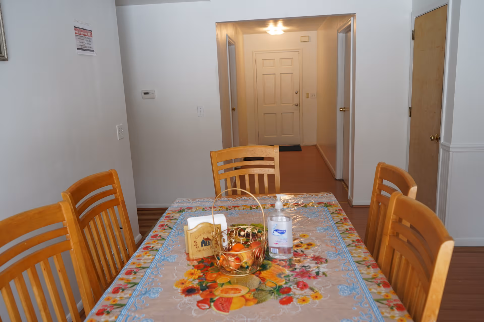 Wood dining table with a colorful tablecloth and chairs in a hallway-adjacent dining room.