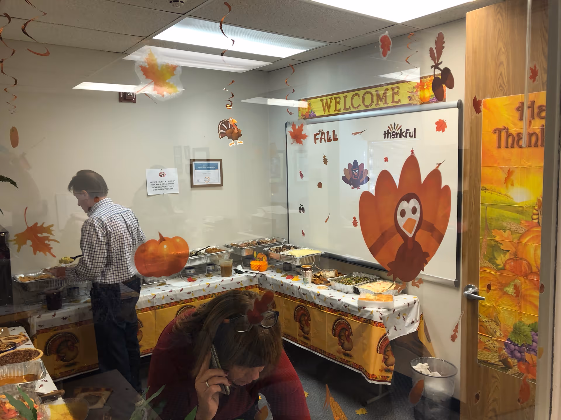 Interior dining area with fall-themed buffet, pumpkins, and leaf decorations along a glass wall.