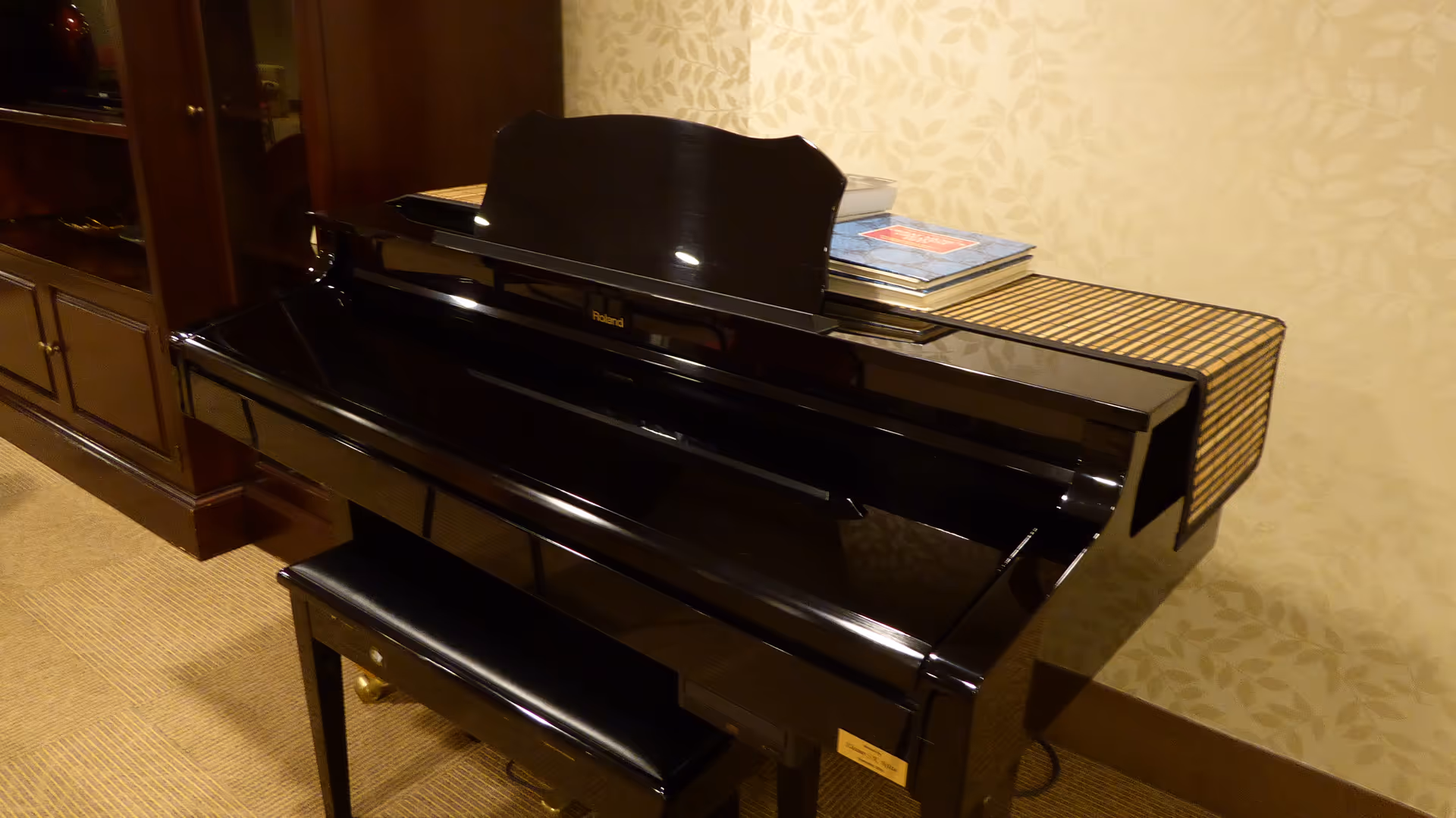 Polished black upright piano with bench sits in a beige patterned-walled living area.