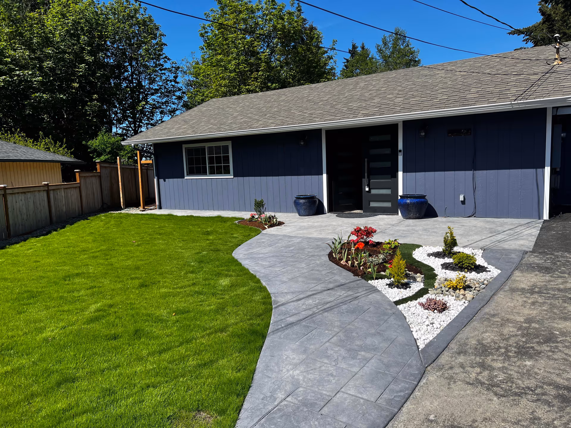 Blue single-story facility facade with manicured lawn, curved concrete walkway, and landscaped flower beds.