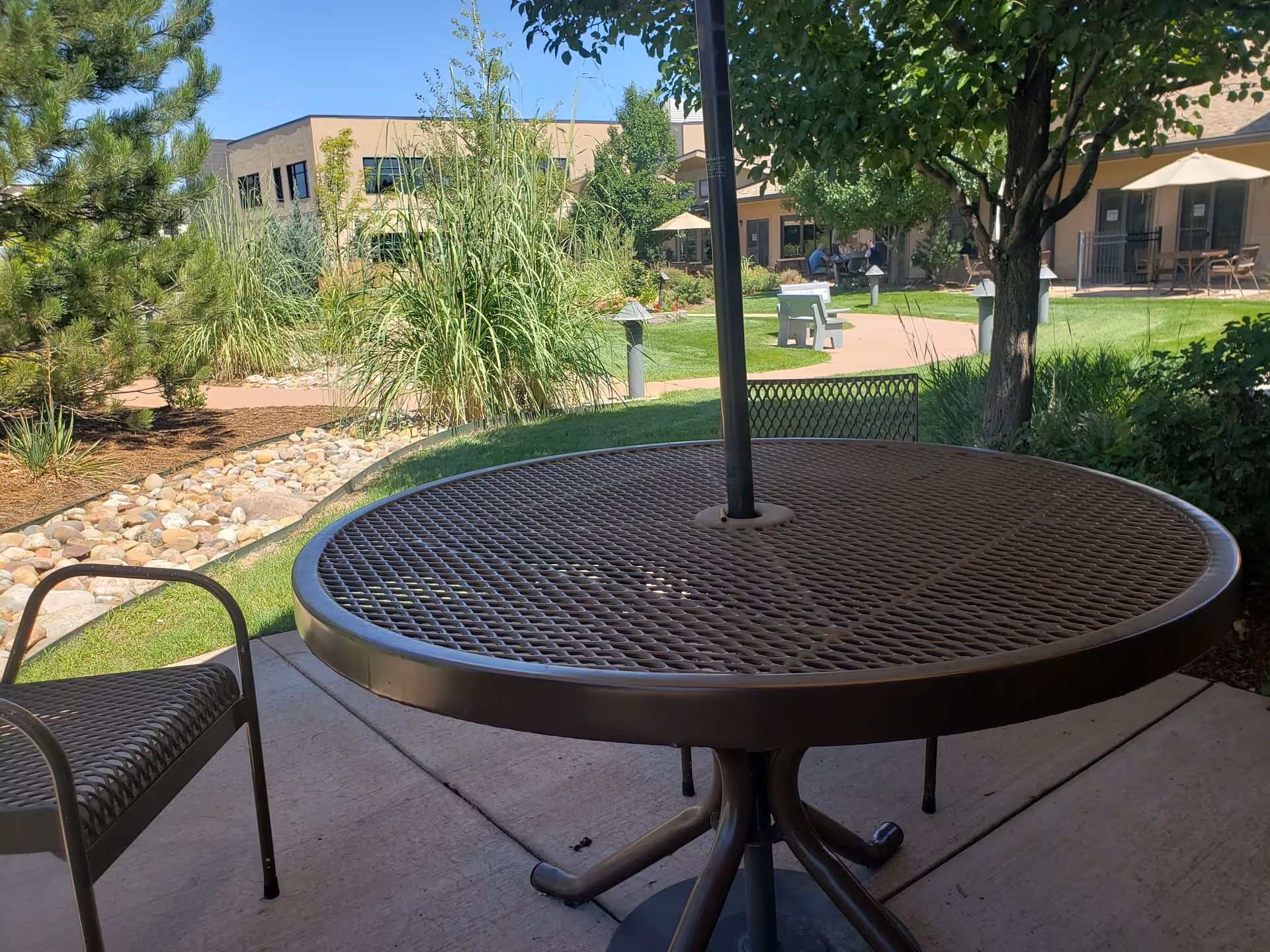 Outdoor patio with round metal table and chairs, by a landscaped courtyard and building.