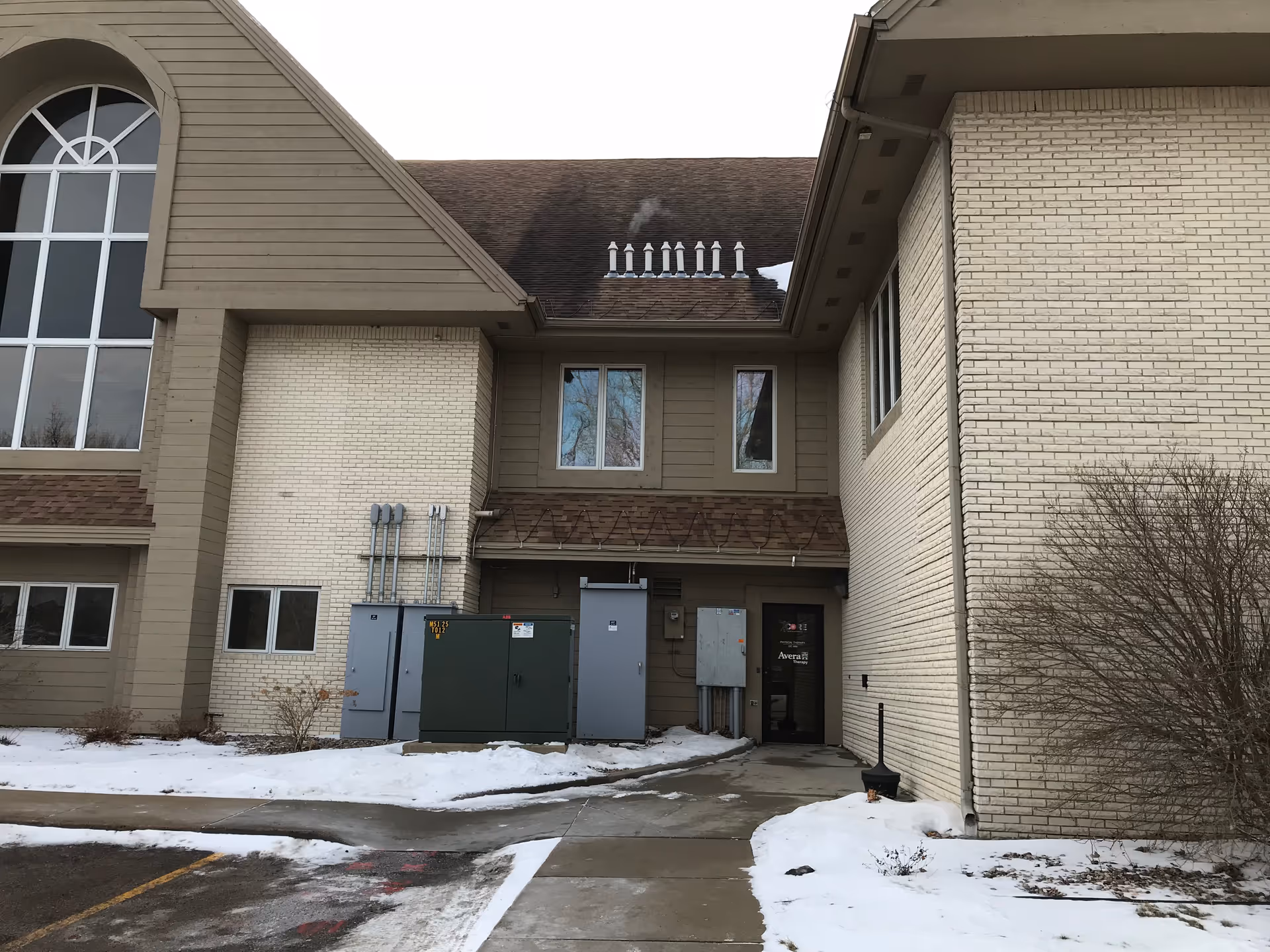 Exterior view of a senior living facility entrance with utility boxes and snowy ground.