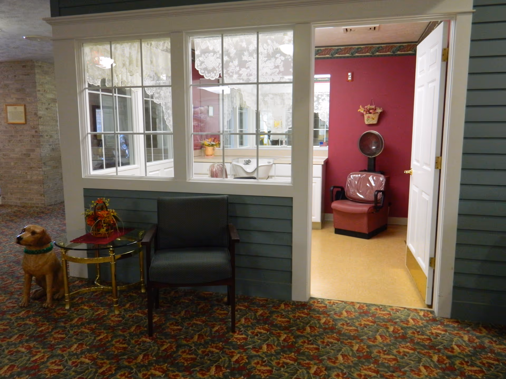 Lobby area of a senior living facility with seating, a dog statue, and a salon room.