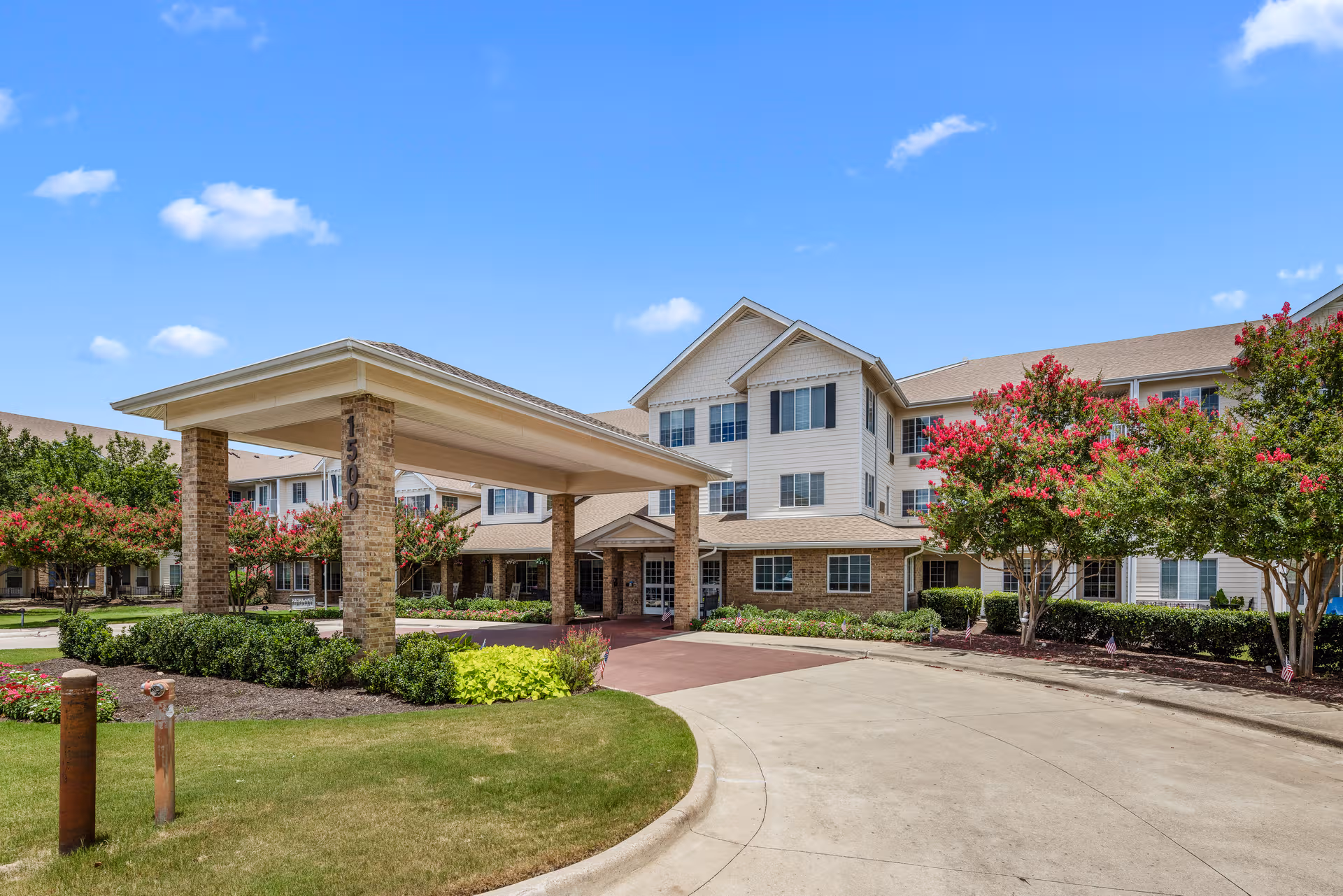 Wide view of Highland Estates Sky Active Living exterior with porte-cochere and landscaped entrance.