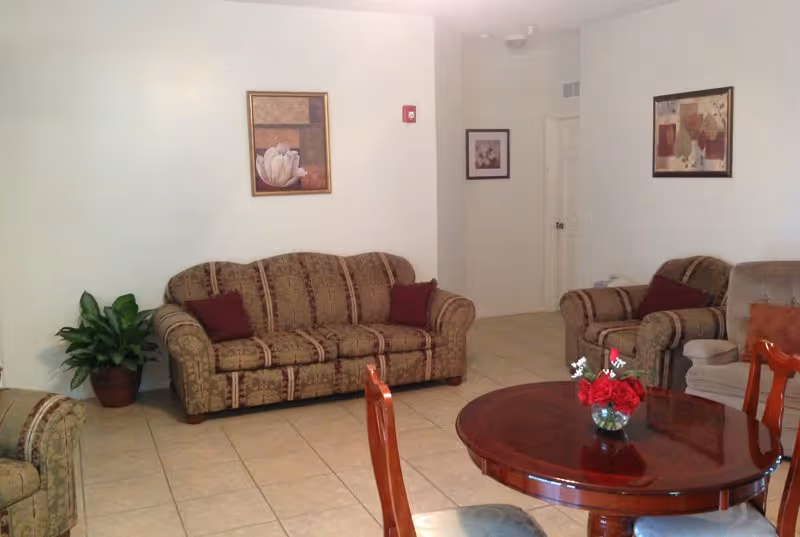 Interior senior living lounge with patterned sofas, a round table, and a potted plant.