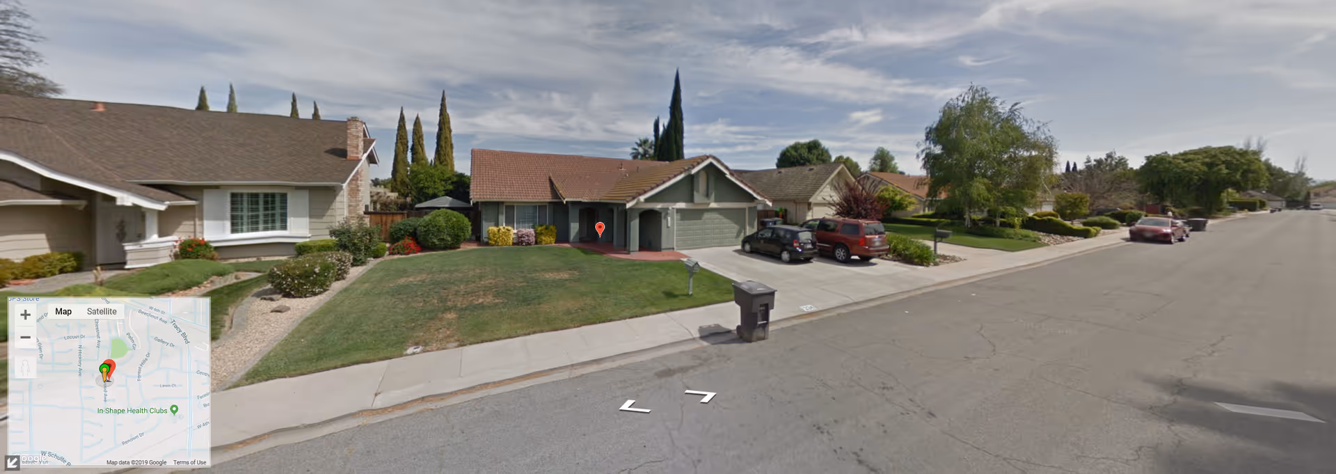 Quiet suburban street with single-story homes, lawns, and a curbside trash bin.