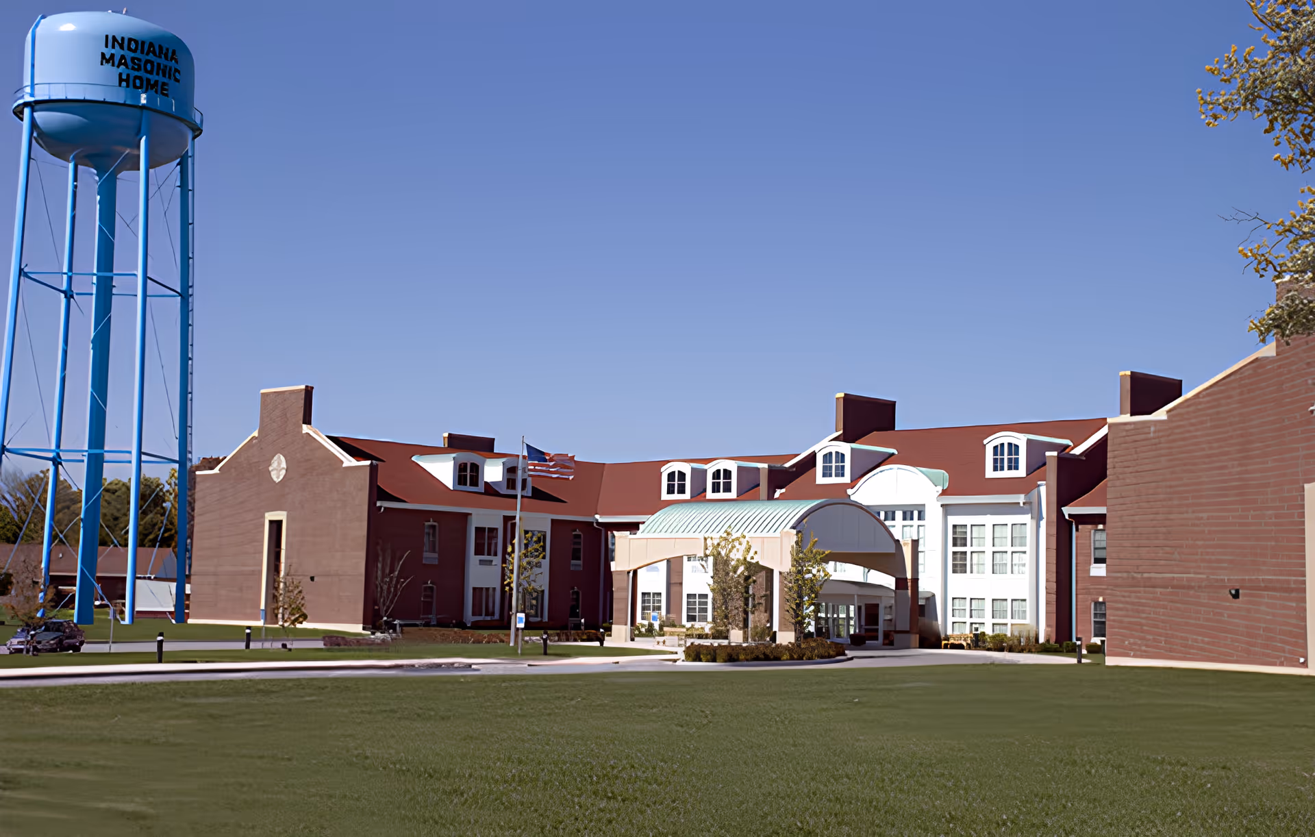 Front entrance of the Indiana Masonic Home Community Center, a large red-brick building with a covered porte-cochère and a blue water tower to the left.