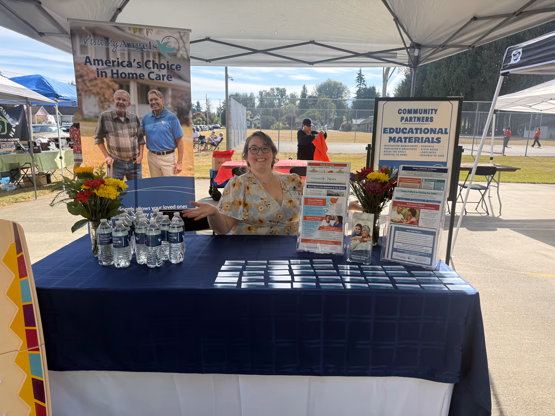 Smiling staff at an outdoor Visiting Angels booth with brochures and bottled water.