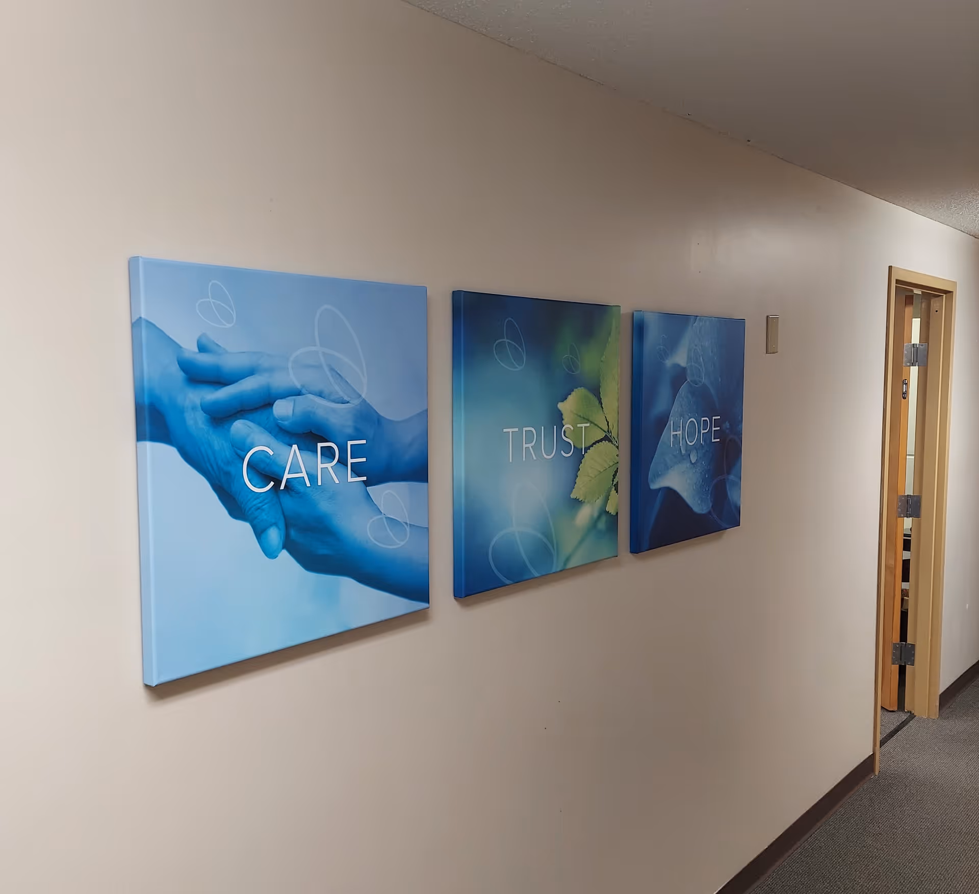 Interior corridor with three blue wall art panels reading CARE, TRUST, HOPE.