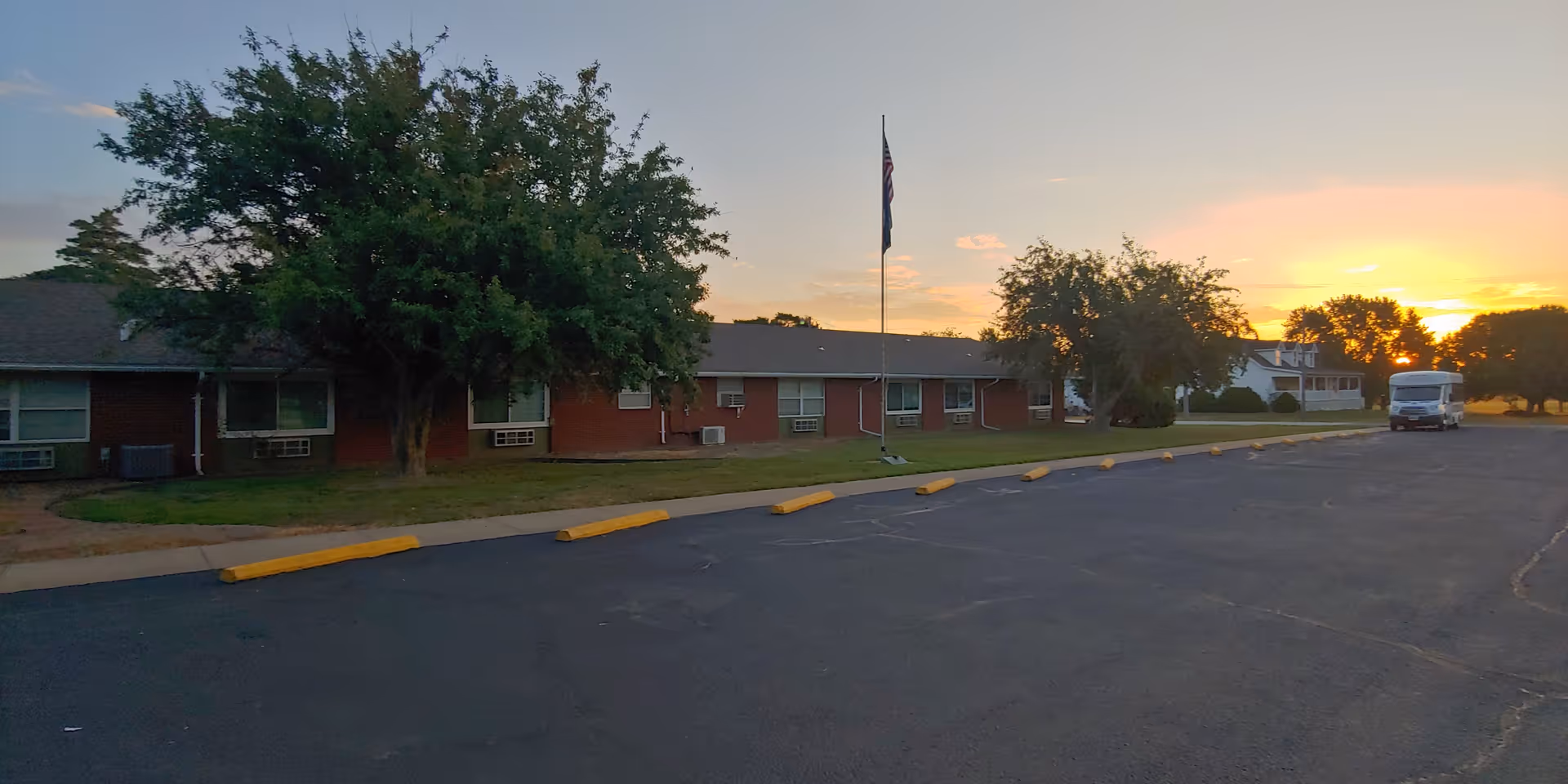 Sunset over Moran Manor exterior, a single-story brick building with a parking lot and flagpole.