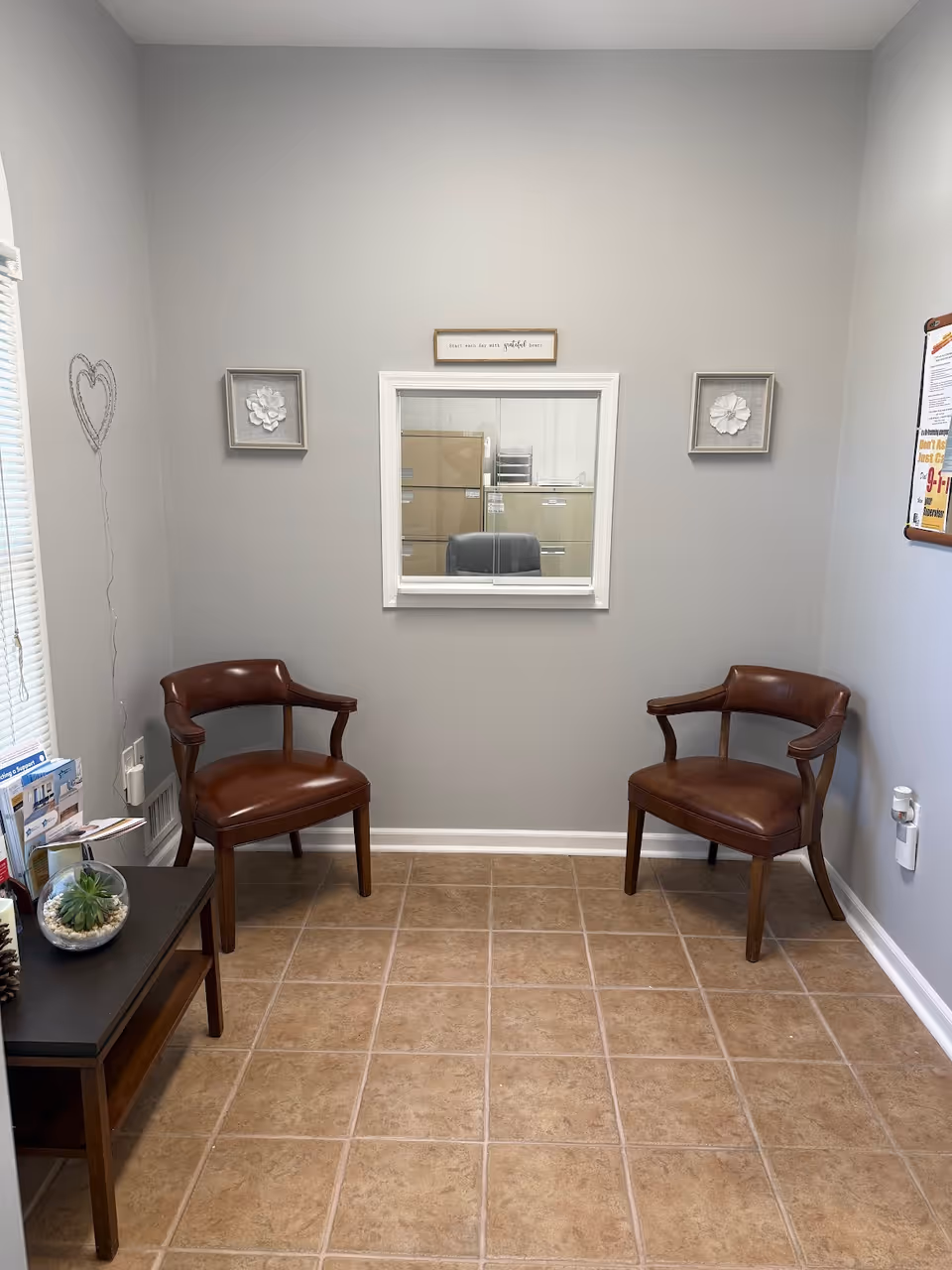 Small waiting area with two brown leather chairs, a windowed office, and a side table.