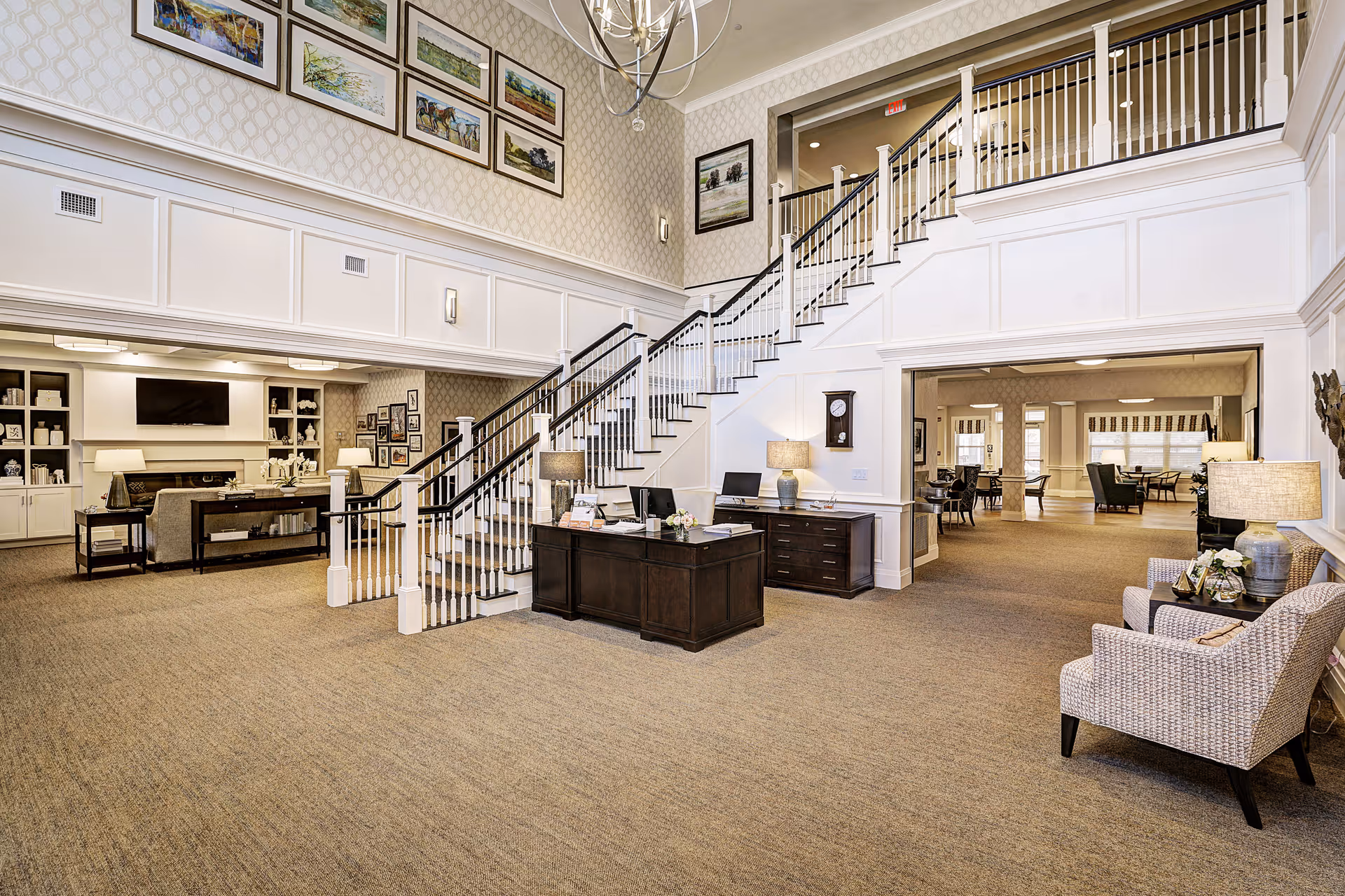Bright, spacious senior living lobby with staircase, reception desk, seating, and wall artwork.