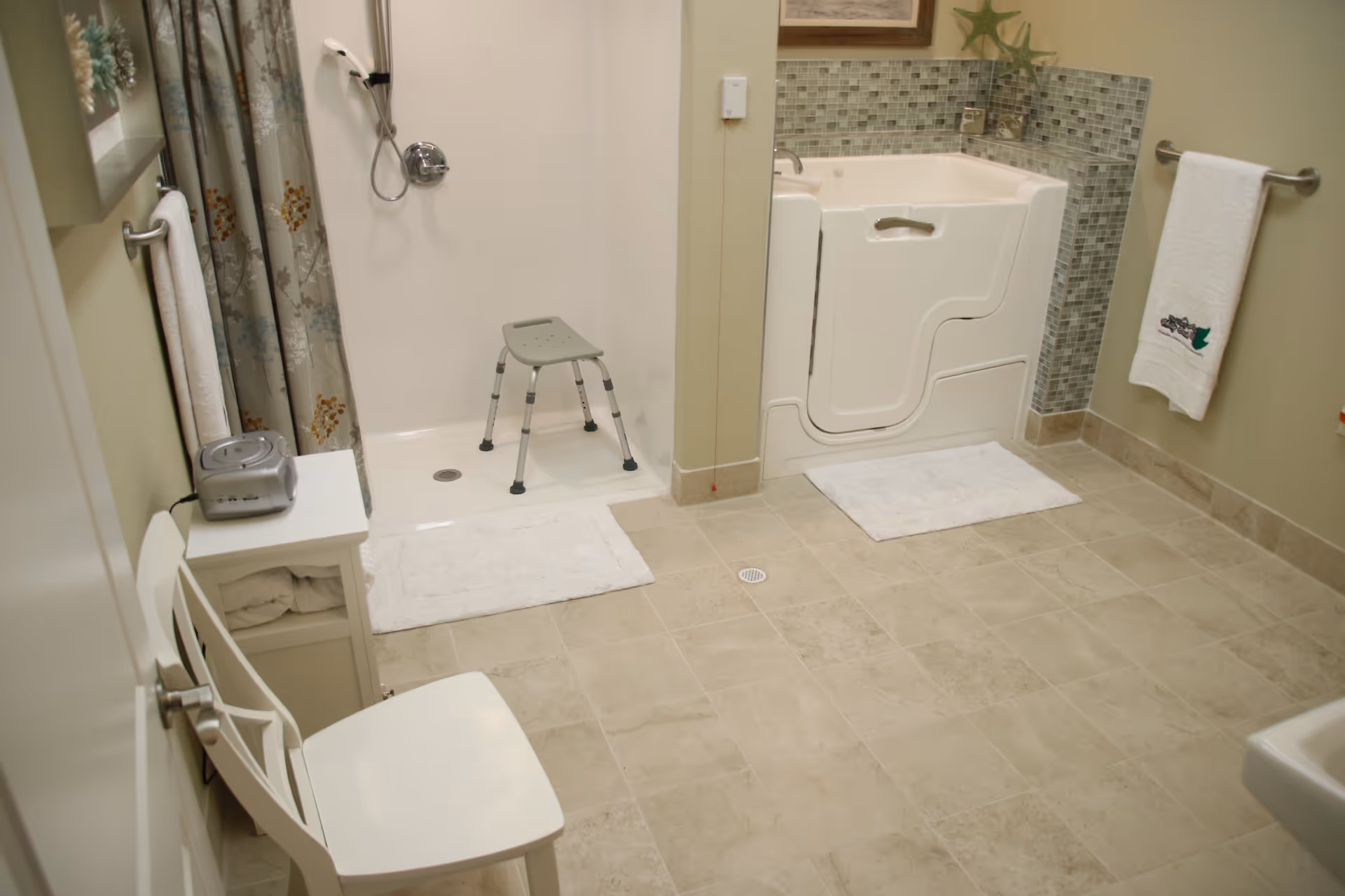 Accessible bathroom with a walk-in tub, shower stall with a transfer bench, grab bars, towels, and tiled floor.