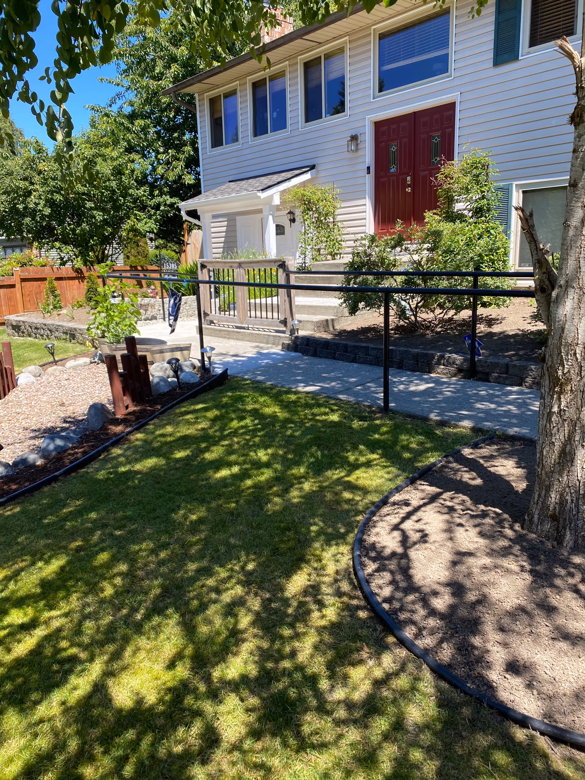 Two-story residential entrance of a senior living facility with a red door and landscaped yard.