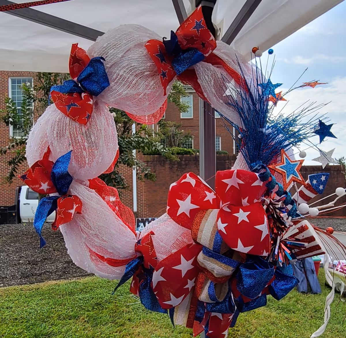 Patriotic wreath with red, white, and blue ribbons hanging near a brick building.